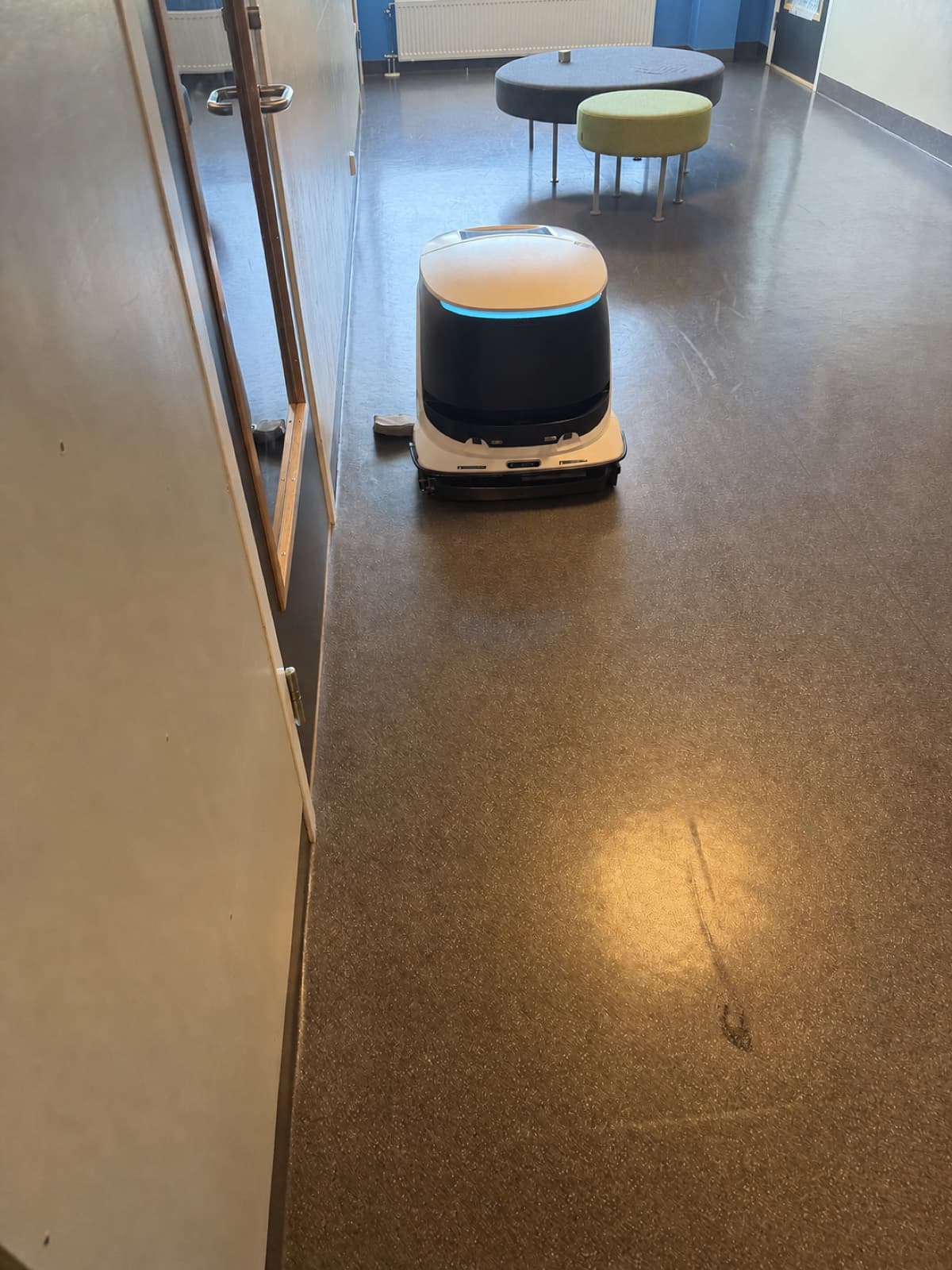 Profesjonell renholdsrobot under utprøving i en norsk korridor med åpne dører og møbler langs veggen.